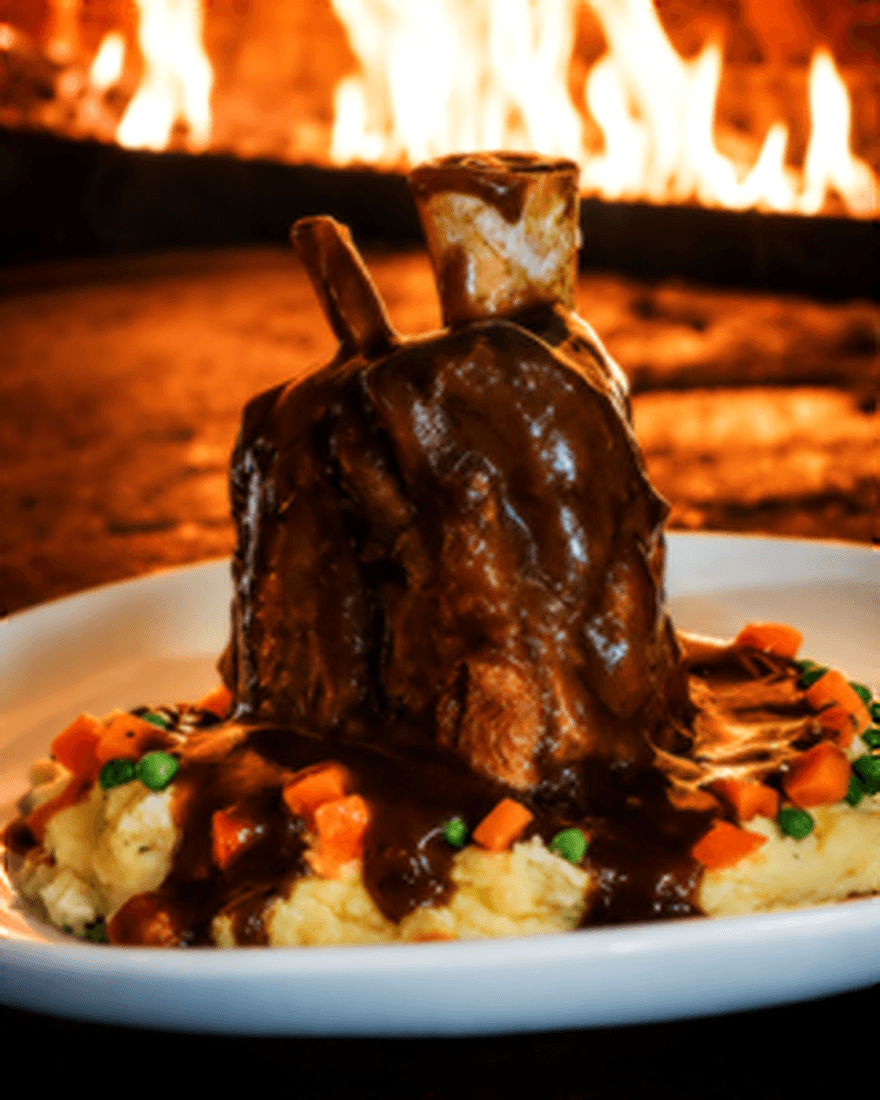 Slow-braised pork shank over mashed potatoes with cabernet gravy, peas and carrots